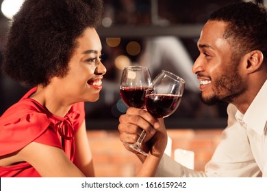 Celebrating Love. Smiling African American Couple Clinking Glasses Drinking Wine Crossing Their Hands During Romantic Valentine Date In Restaurant