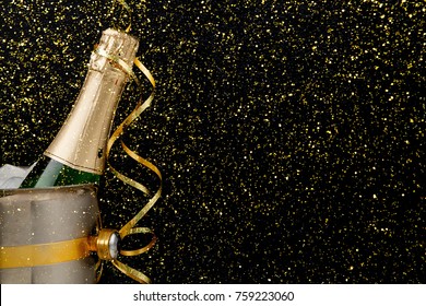 Celebrating New Year, Birthday, Xmas Party. Bottle Of Champagne In A Bucket And Colorful Tinsel On Black Backgroud With Golden Glitters, Copy Space. Mockup For Postcard