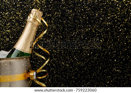 Celebrating new year, birthday, xmas party. Bottle of champagne in a bucket and colorful tinsel on black backgroud with golden glitters, copy space. Mockup for postcard