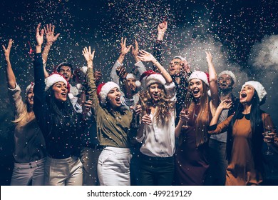 Celebrating New Year together. Group of beautiful young people in Santa hats throwing colorful confetti and looking happy - Shutterstock ID 499219129