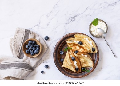 Celebrating Pancake day, healthy breakfast. Delicious homemade crepes with blueberries and riccota on a stone tabletop. Top view flat lay. Copy space.