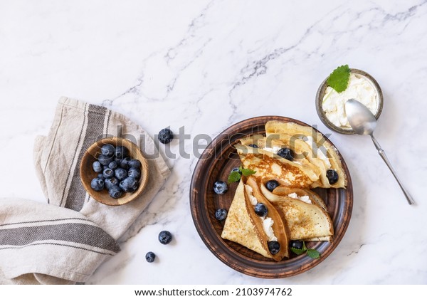 Celebrating Pancake day, healthy breakfast.\
Delicious homemade crepes with blueberries and riccota on a stone\
tabletop. Top view flat lay. Copy\
space.