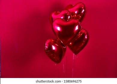 Celebrating Saint Valentine's Day with heart shaped red foil air balloon. Gift for loved woman on special occasion with romantic symbols, Women`s day. Close up, copy space, background, isolated.