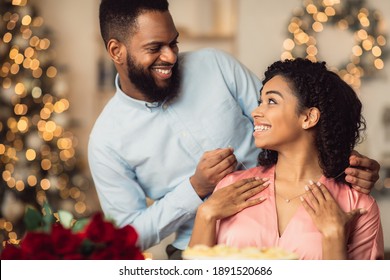Celebrating Special Day. Smiling black man wearing jewel necklace on his happy young woman. Beautiful african american family spending time together in luxury cafe, having romantic dinner