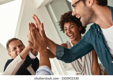 Celebrating success. Business people giving each other high-five and smiling while working together in the modern office