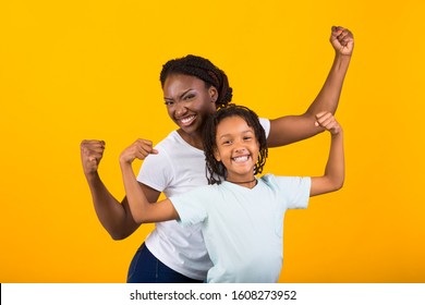 Celebrating Success. Cheerful black mother and daughter holding hands up for victory isolated on yellow background