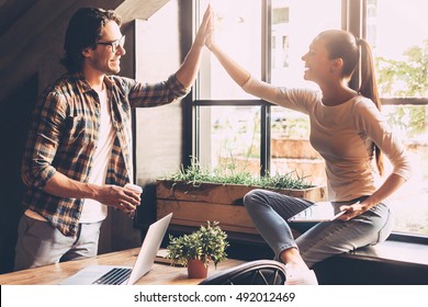 Celebrating success. Cheerful young man and woman giving high-five while having coffee break in creative office 