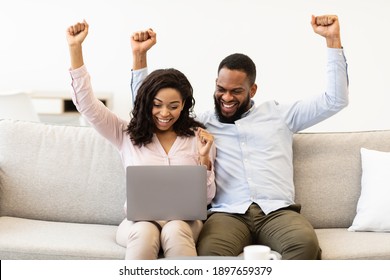 Celebrating Success. Overjoyed African American Man And Woman Happy With Money Win, Satisfied About Success. Black Couple Shaking Fists And Looking At Laptop Computer, Sitting On The Couch At Home