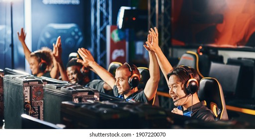 Celebrating success. Team of happy proffesional cyber sport gamers giving high five to each other while participating in eSports tournament - Shutterstock ID 1907220070
