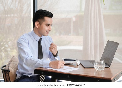 Celebrating success. Young asian business man working with laptop, tablet and papers on desk at office. He feeling good and happy. - Shutterstock ID 1932544982