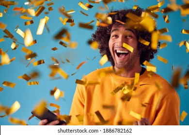 Junger Mann mit dem Preis für das Mobiltelefon feiern und mit Gold Confetti im Studio duweren