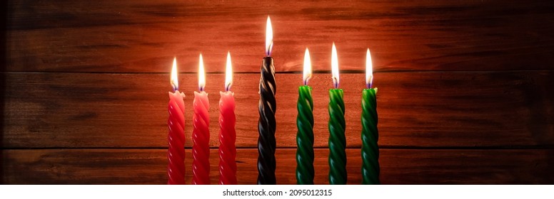 Celebration of African American Kwanzaa festival. Seven burning candles red, black and green in traditional Kinara candlestick. Symbols of African heritage on wooden background. Banner format - Powered by Shutterstock