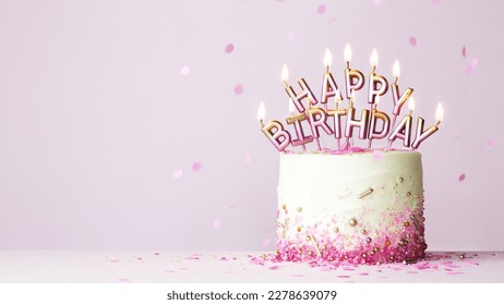 Celebration birthday cake with pink and gold birthday candles spelling happy birthday against a pink background