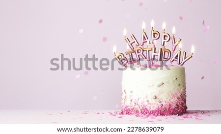 Celebration birthday cake with pink and gold birthday candles spelling happy birthday against a pink background