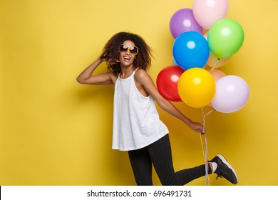 Celebration Concept - Close up Portrait happy young beautiful african woman with white t-shirt running with colorful party balloon. Yellow Pastel studio Background.