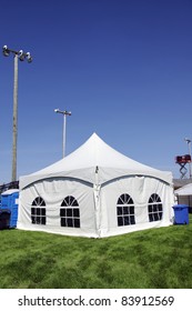 Celebration Or Event: White Tent On Soccer Field With Lighting Ready For Guests In Case Of Rain With Sound System On Lift In The Background, Portable Toilet And Bins For Disposal.