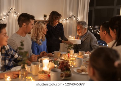 Celebration And Family Concept - Happy Grandfather Blowing Candles On Birthday Cake At Dinner Party At Home