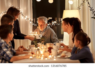 Celebration And Family Concept - Happy Grandfather Blowing Candles On Birthday Cake At Dinner Party At Home