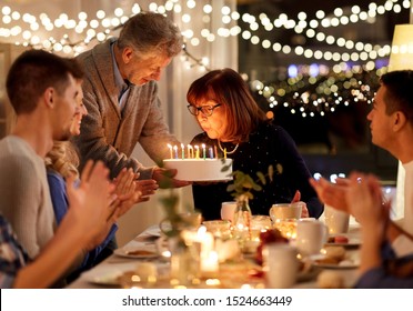 Celebration And Family Concept - Happy Grandmother Blowing Candles On Birthday Cake At Dinner Party At Home