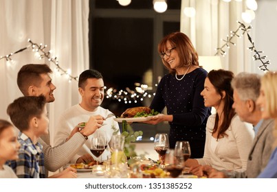 Celebration, Holidays And People Concept - Happy Senior Woman Offering Roast Chicken To Family Having Dinner Party At Home