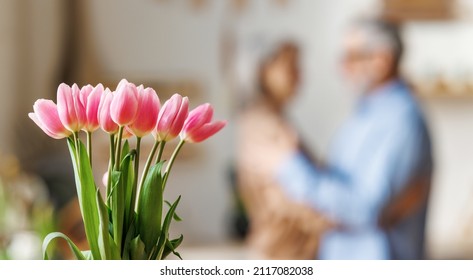 Celebration of love. Beautiful bouquet of fresh pink tulips against dancing senior couple on blurred background, elderly man and woman celebrating Anniversary day at home. Valentine's Day and March 8 - Powered by Shutterstock