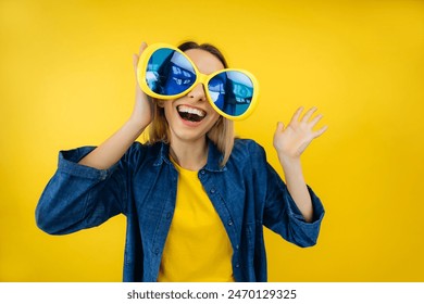 Celebration and party. Having fun. Young pretty woman laughing wearing oversized party glasses wave hello. Colorful studio portrait with yellow background. - Powered by Shutterstock