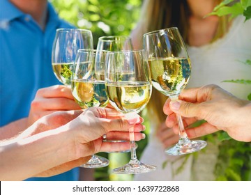 Celebration. People Holding Glasses Of White Wine Making A Toast. Family Outdoor Dinner In The Garden In Summertime At Sunset. Picnic Food And Drink Concept 
