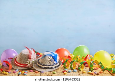 Celebratory hats with feathers stuck in them and multicolored balloons sitting on rustic wood plank table