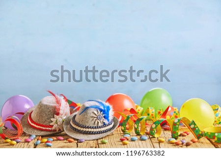 Celebratory hats with feathers stuck in them and multicolored balloons sitting on rustic wood plank table