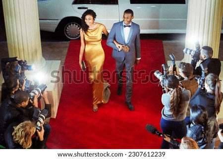 Celebrity couple arriving at red carpet event being photographed by paparazzi