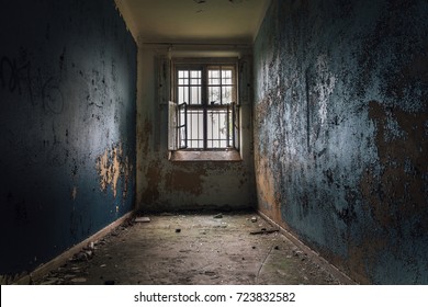 Cell from an old closed down mental institution with flaked of painting on the thick concrete walls and bars over the windows