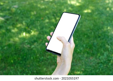 Cell Phone With Blank White Screen. Woman Hand Holding Using Mobile At Outdoor. Blurred Green Grass In The Background With Copy Space. Mockup Image.