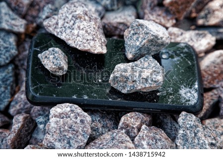 Cell phone with broken glass on gravel granite stones, unbreakable gadget.