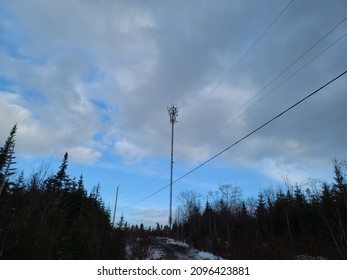 A Cell Phone Tower Under A Cloudy Sky. The Ground Below Is Covered With A Light Dusting Of Snow.