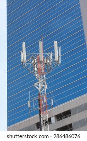 Cell Site, Telecommunications Radio Tower Or Mobile Phone Base Station With Atop The Antennas With Building Background.