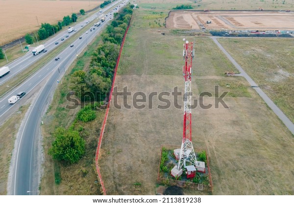 Cell site of telephone tower with 5G base\
station transceiver by highway with traffic move drive cars. Aerial\
view of telecommunication antenna\
mast