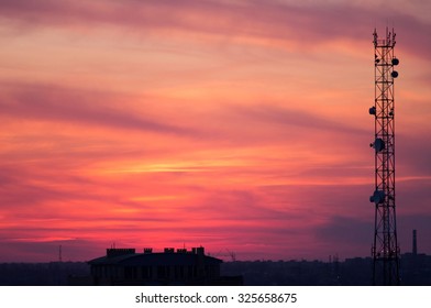 Cell Tower And The City Of Construction On A Background Of Red Clouds After Sunset