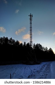 A Cell Tower Stands On The Ground Near The Forest