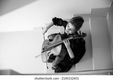 cellist sits on the stairs and plays the cello, enjoys playing music, top view, black and white image, suitable for a poster or poster