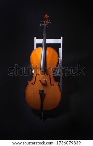 Cello leaning on white chair on black background