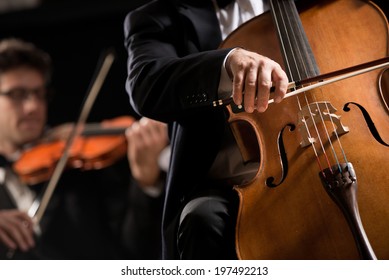 Cello Professional Player With Symphony Orchestra Performing In Concert On Background.