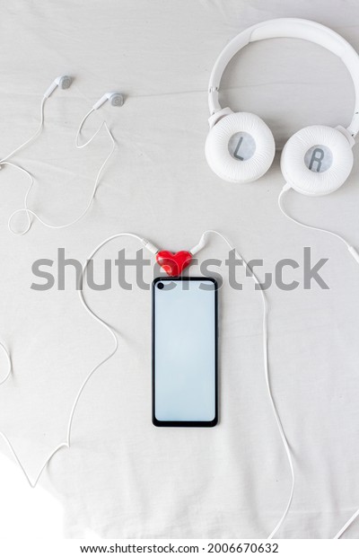 Cellphone with an earphone and headphone plugged in\
together by a heart shapped audio divider. Romantic concept. Top\
view. Flat lay.