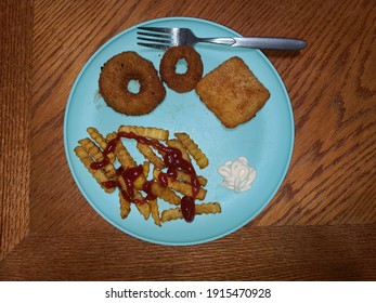A cellphone image of a salted baked piece of breaded fish with fresh fried onion rings and French fries covered in ketchup and salt served on a teal blue plate on a wooden table top with a fork