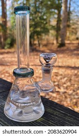 A cellphone image of a semi clean clear glass bong aka a water pipe used for smoking marijuana in it outside on a wooden table during a fall day