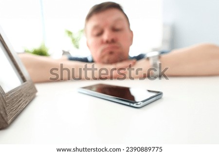 Cellphone lying on table with pensive man in background waiting for call or out of network coverage closeup