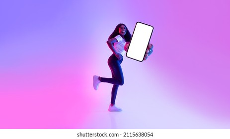 Cellphone Screen Mockup. Joyful Young Black Woman Running With Empty Mobile Phone, Promoting New App, Advertising Cool Website In Neon Light, Copy Space For Online Advertisement