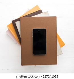 cellphone with stack of book over white table