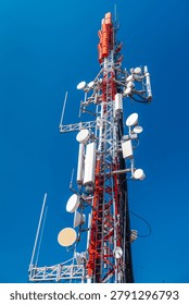 Cellular communication tower with multiple antennas and transmitters against clear blue sky