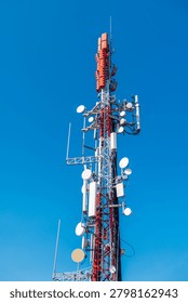 Cellular communication tower with multiple antennas and microwave dishes against clear blue sky, modern telecommunications infrastructure