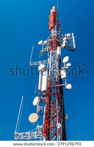 Cellular communication tower with multiple antennas and transmitters against clear blue sky